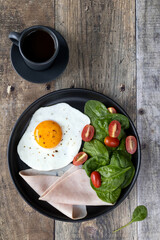 Continental breakfast: fried eggs, ham, tomatoes, spinach, coffee on a wooden table. Top view, copy space.