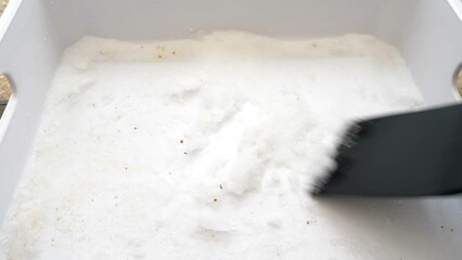 Closeup of a man’s hand using a soft kitchen tool to scrape accumulated frost from the bottom of a freezer drawer.