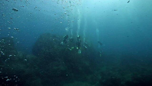 Under water film of rising air bubbles and a cluster of scuba divers in the background - Sail Rock island in Ssouthern Thailand