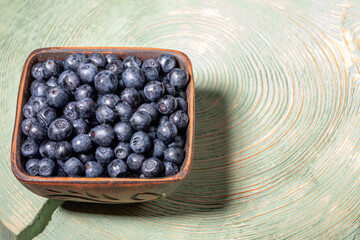 Wild forest blueberries in brown ceramic bowl on green cross wooden cut with annual rings.