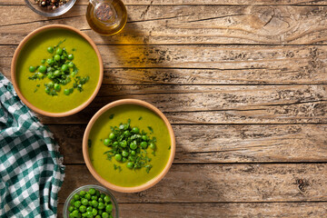 Green pea soup in a wooden bowl on rustic wooden table. Top view. Copy space