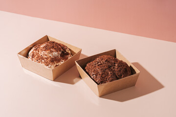 Two turtle cakes in paper box with transparent lid on pink background.