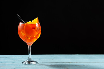 Glass of aperol spritz cocktail on blue wooden table and black background. Copy space