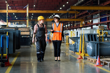 Two young workers of modern industrial factory having discussion of work while moving along aisle...