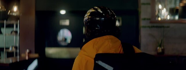 TRACKING Food delivery courier in bicycle helmet entering the restaurant to pick up order for delivery. Shot with 2x anamorphic lens