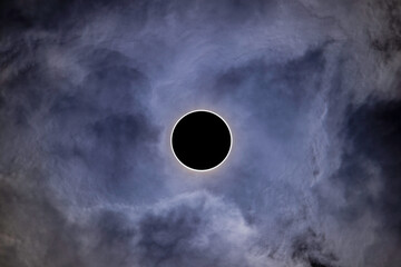 Zachmurzone niebo. W centrum kadru tarcza słoneczna przysłonięta czarną tarczą księżyca. Całkowite zaćmienie słońca.