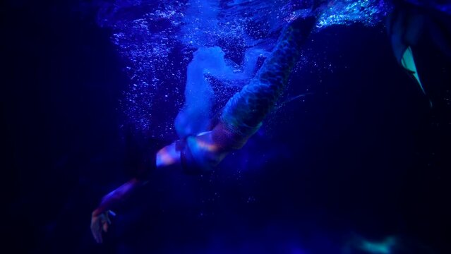 the mermaid swims with pleasure in the blue water with bubbles. the streaks of red light are sliding. the general plan
