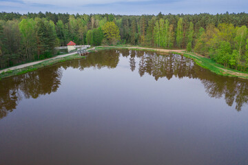 Fototapeta na wymiar Zbiornik wodny, zalew położony w lesie. Brzegi porośnięte drzewami. Widoczna jest mała elektrownia wodna. Zdjęcie z drona.