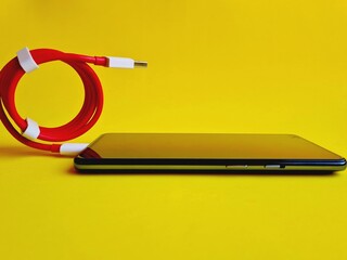 smartphone connected to red cable resting on yellow background