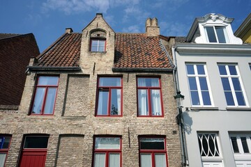 Schönes alte Haus mit Fassade aus Naturstein in Naturfarben und roten Fensterrahmen vor blauem...