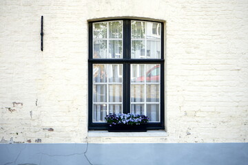 Weiße Fassade mit altem Sprossenfenster und Blumenkasten mit blauen Blumen auf der Fensterbank im...