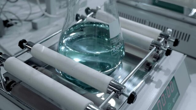 Laboratory shaker mixes solution in glass flack for products in the medical, chemical, cosmetic industries. Closeup. Shot in motion