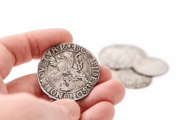 Male hand holding old silver thaler with lion on reverse. Old coins on white background. Lion...