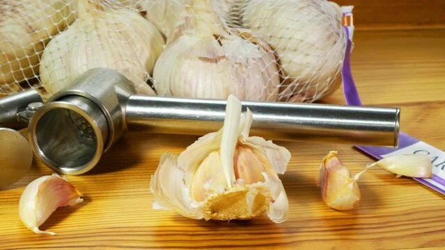 Closeup dolly shot of garlic heads / bulbs in a retail pack, with some cloves next to a steel press tool.