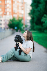 Plus size girl with long brown hair with dog on sidewalk, young woman and black poodle pet