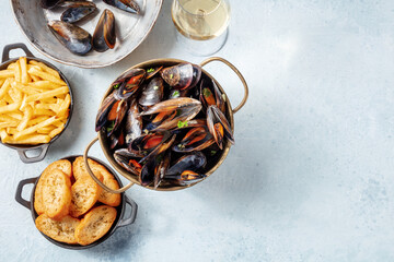 Cooked mussels with toasted bread, French fries, and white wine, overhead flat lay shot on a slate background with a place for text