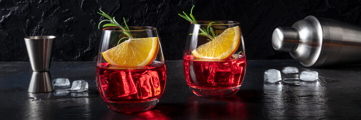 Campari cocktails with fresh oranges, rosemary, a jigger and a shaker, a panorama on a black slate...