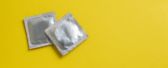 Condoms package on yellow background. A condom use to reduce the probability of pregnancy or...