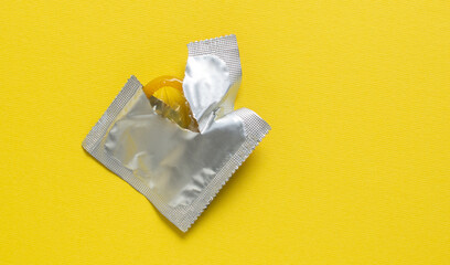 Opened condom and condom in pack on a yellow background. A condom use to reduce the probability of...