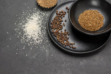 Allspice on black porcelain plate. Coriander seeds in black bowl.