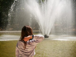 Petite fille de dos devant un bassin avec fontaine, dans un parc