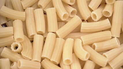 Raw penne pasta in bowl on wooden background.