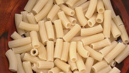 Raw penne pasta in bowl on wooden background.