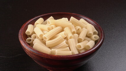 Raw penne pasta in bowl on wooden background.