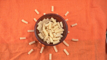 Raw penne pasta in bowl on wooden background.