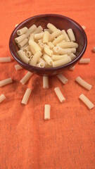 Raw penne pasta in bowl on wooden background.