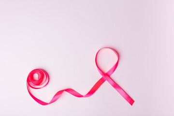 Red ribbon as a symbol of solidarity for people living with HIV or AIDS on a pink background. World...