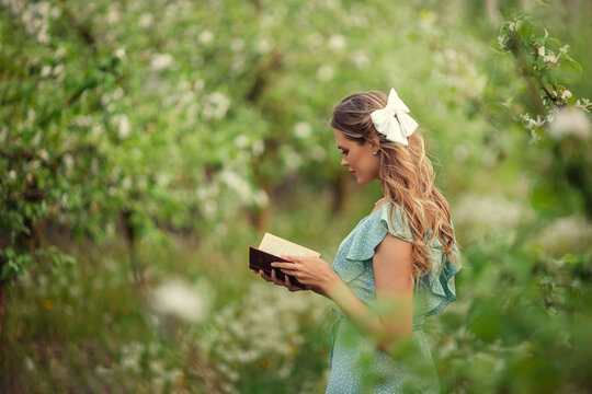 beautiful young woman in a romantic dress reads a second book in spring in a blooming garden