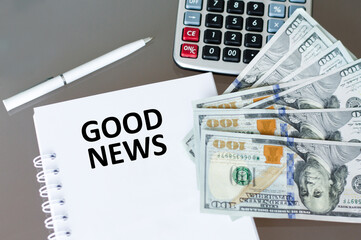 Good News text on a notepad on a table next to a pen, calculator and money