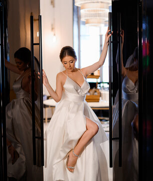Elegant fiancee in wedding gown posing between doors