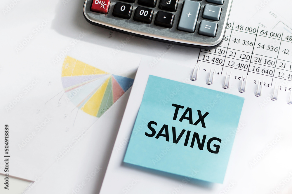 Poster card with text tax saving text on a blue card that lies on a notebook on the background of a table, 