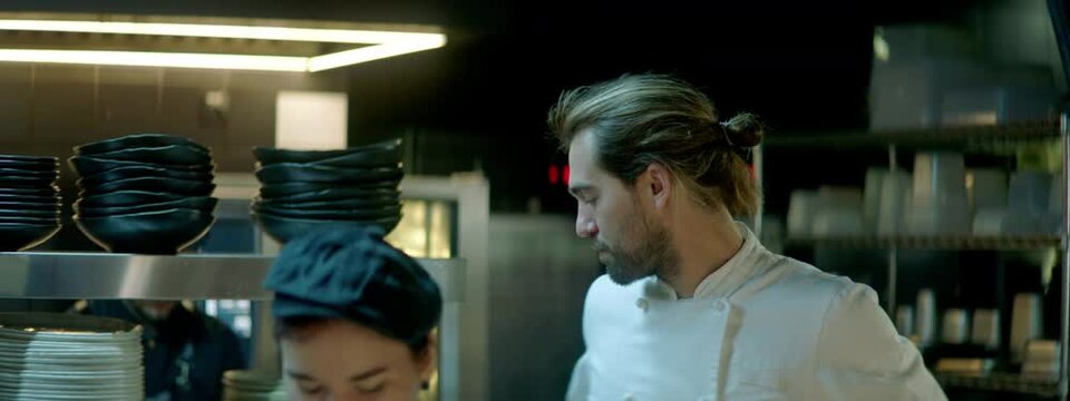 TRACKING Chef checking new orders on a display, walking through busy commercial restaurant kitchen. Shot with 2x anamorphic lens