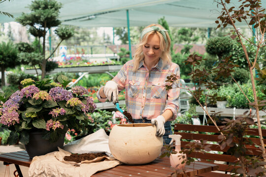 Woman planting flower in pot using dirt in garden center