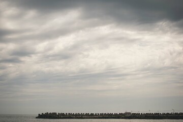 Heavy clouds over the sea with sun light poring through on the sea shore line with pier line...