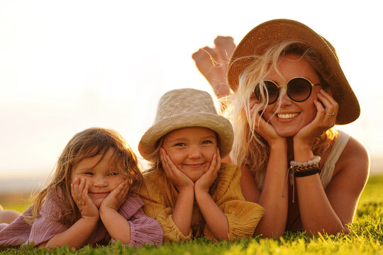 Happy woman relaxing with her two daughters outdoor on the meadow, lying, smiling. Mother's day. Children's day.