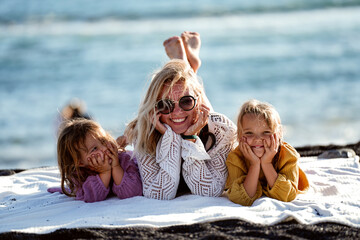Fototapeta na wymiar Happy woman relaxing with her two daughters outdoor on the beach, lying, talking and smiling. Mother's day. Children's day.