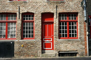 Fassade mit altem Mauerwerk in Naturfarben mit roten Fenstern und schöner Haustür in leuchtendem...