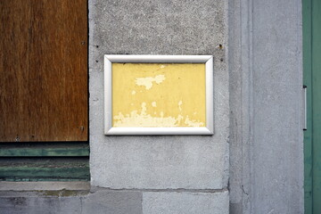 Obraz premium Verwahrlostes heruntergekommenes Schild mit gelbem Hintergrund und silbernem Rahmen auf grauem Beton in den Gassen der Altstadt von Brügge in Westflandern in Belgien