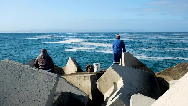 Local fishermen standing on dolosse of harbour to try and catch a fish