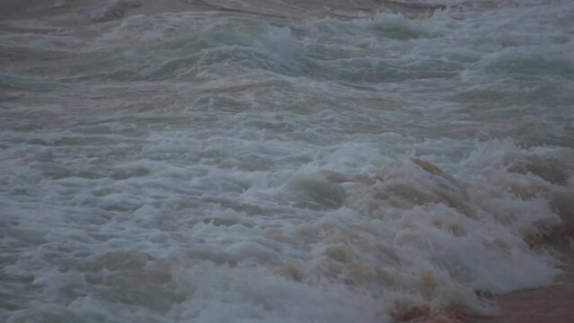 Closeup slow motion of frothy sea wave on the shore at Baga beach in Goa, India. Foamy sea wave crashes on the beach after sunset. Natural wave background.	