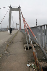 One wanderer walks along a pedestrian cable-stayed bridge against the background of rusty steel...