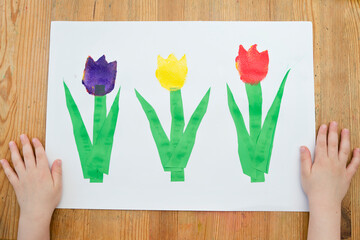 Kid painting with gouache a spring flower. Boy produces colored tulips for mommy. Children's...