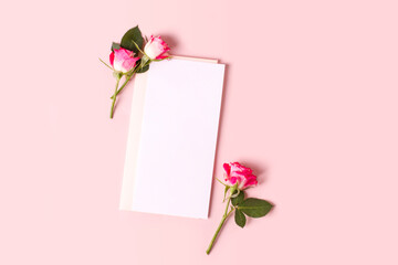 Invitation or greeting card mockup with a blank sheet and some delicate pink roses on a pastel pink...