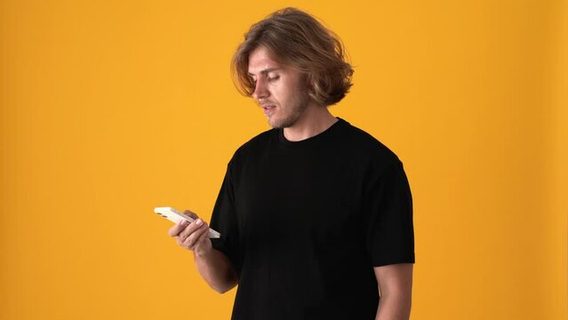 Pensive blond man texting by phone in the yellow studio