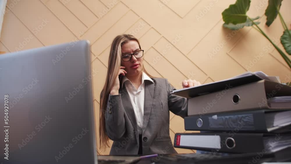 Poster office worker woman works talking on smartphone and sorting through sheets of documents sitting at d