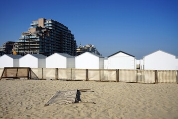 Traditionelle weiße Strandkabinen und moderne Hochhaus Architektur am Strand der Nordsee bei blauem Himmel und Sonnenschein in Knokke-Heist bei Brügge in Westflandern in Belgien